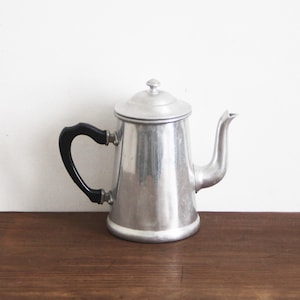 May include: A silver aluminum coffee pot with a black plastic handle. The pot has a rounded body and a spout on the side.