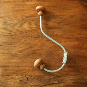 May include: A light blue metal coat hook with two wooden knobs. The hook is bent into an 'S' shape and is mounted on a wooden surface.