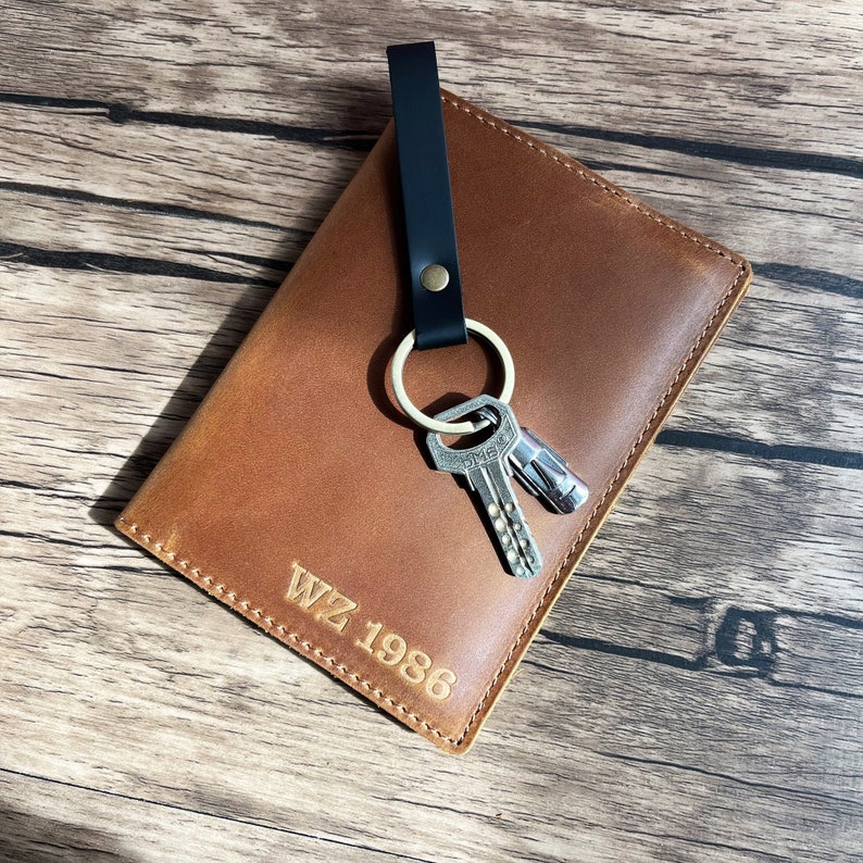 May include: A brown leather key holder with a black strap and a key ring with two keys. The key holder has the text "WZ 1986" embossed on the front.