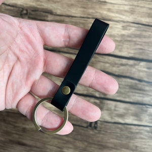 May include: A black leather keychain with a brass key ring. The keychain is about 5 inches long.