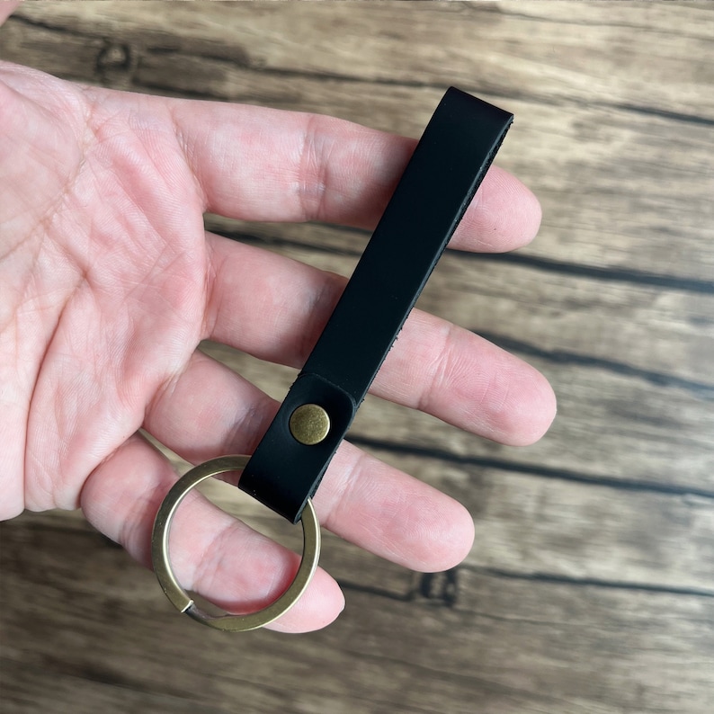 May include: A black leather keychain with a brass key ring. The keychain is about 5 inches long.