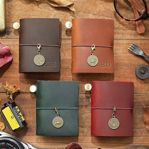 May include: Four brown leather journals with zodiac charms. Each journal has a different colour and a different zodiac sign charm. The charms are for Aries, Taurus, Cancer, and Aquarius. The journals are on a wooden surface.