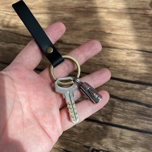 May include: A black leather keychain with a brass key ring and a silver key with a D.M.S. logo. A silver charm with a face is attached to the key ring.