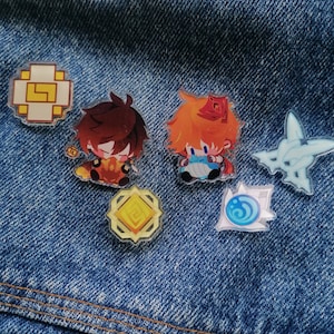 Könnte beinhalten: Fünf bunte Emaille-Pins mit Comicfiguren und geometrischen Mustern. Die Pins befinden sich auf einem blauen Jeans-Hintergrund.