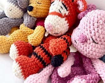 May include: A collection of handmade crochet plush toys in various colors. The toys include a gray donkey, a yellow bear, an orange tiger, and a pink pig. Each toy has closed eyes, suggesting they are sleeping. The toys are made of soft, textured yarn.