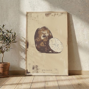 Könnte beinhalten: Ein rechteckiger Wandkunstdruck mit einer dunkelbraunen Illustration einer ganzen Kartoffel und einer aufgeschnittenen Kartoffelhälfte auf hellbeigem Hintergrund. Das Wort potato ist in kleinen, dunklen Kleinbuchstaben unten gedruckt.