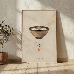 May include: A framed wall art print on a light beige background featuring a dark brown bowl filled with white congee, topped with orange garnish and green herbs. Below the bowl are orange paint splatters and the text congee in lowercase.