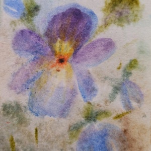 May include: Watercolor painting of a purple and blue flower with yellow and orange accents. The flower is painted on a light brown background.