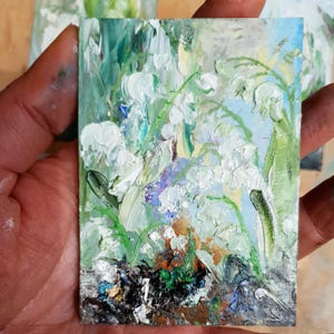 K&ouml;nnte beinhalten: Ein kleines, rechteckiges &Ouml;lgem&auml;lde, das wei&szlig;e Maigl&ouml;ckchenbl&uuml;ten mit gr&uuml;nen Bl&auml;ttern und St&auml;ngeln darstellt. Das Kunstwerk verwendet dicke Pinselstriche und eine Palette aus Wei&szlig;, Gr&uuml;n, Blau und Braun.