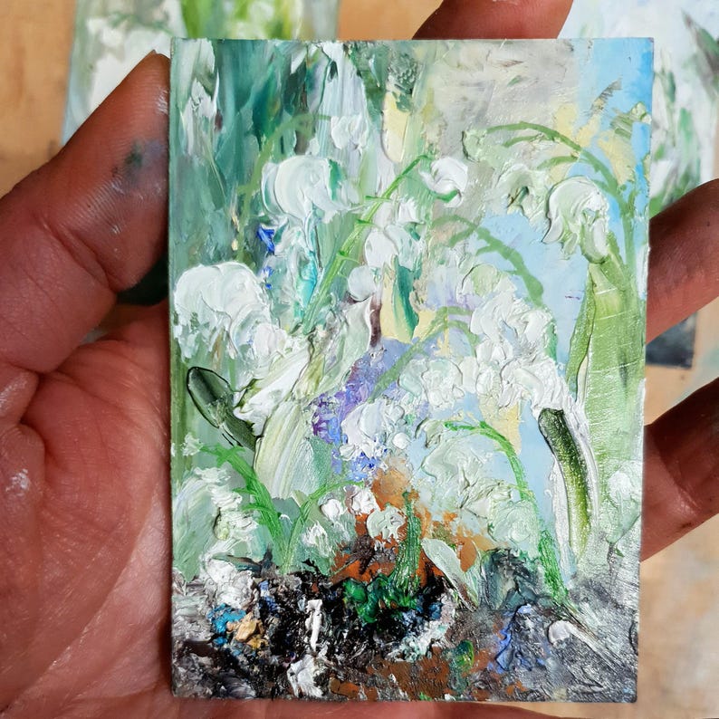 K&ouml;nnte beinhalten: Ein kleines, rechteckiges &Ouml;lgem&auml;lde, das wei&szlig;e Maigl&ouml;ckchenbl&uuml;ten mit gr&uuml;nen Bl&auml;ttern und St&auml;ngeln darstellt. Das Kunstwerk verwendet dicke Pinselstriche und eine Palette aus Wei&szlig;, Gr&uuml;n, Blau und Braun.