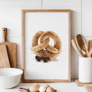 Può includere: Una stampa ad acquerello incorniciata di un personaggio di pretzel sorridente. Il pretzel è di colore marrone chiaro con dettagli marrone scuro e piccoli piedi neri. L'opera d'arte è in una cornice di legno, su una parete piastrellata bianca.