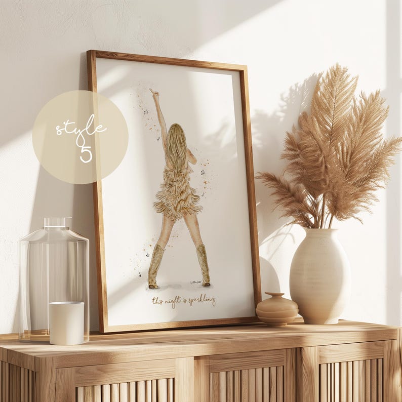 May include: A framed watercolor print featuring a woman in a fringed dress and boots, raising her arm. The artwork is in a wooden frame and includes the text "This night is sparkling." A beige circle with the text "style 5" is in the upper left corner.