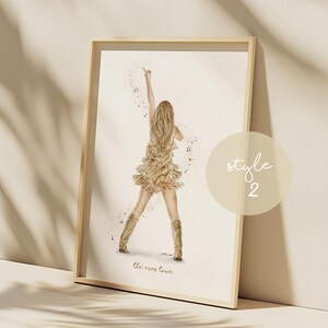 May include: Watercolor print of a performer on stage, wearing a fringed dress and boots, with an arm raised. The artwork is framed in a light wood frame. The text "the eras tour" is at the bottom of the image.