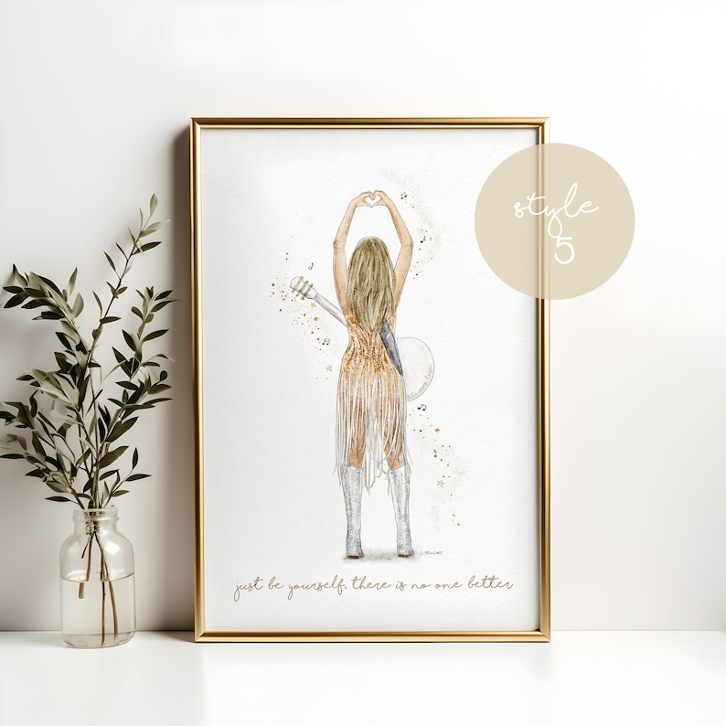 May include: A framed art print featuring a blonde figure seen from behind, wearing a gold fringed dress and white boots, holding a guitar and making a heart shape with hands. The text reads, "just be yourself. there is no one better."