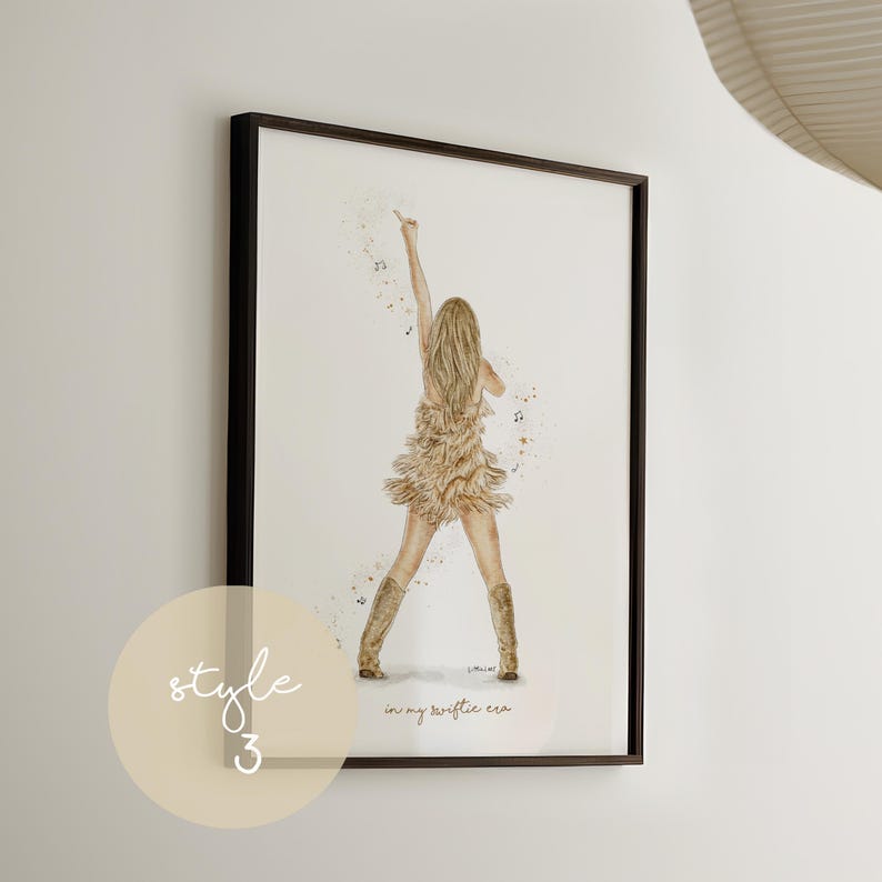 May include: Framed art print featuring a watercolor illustration of a person on stage, wearing a fringed dress and boots, with their arm raised. The print includes the text "in my swiftie era" and is framed in a black frame. A light beige circle with the text "style 3" is in the lower left corner.