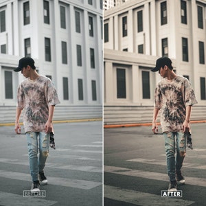 May include: A person wearing a tie-dye shirt and ripped jeans stands in front of a building. The person is wearing a black baseball cap and has their hands in their pockets. The building is made of concrete and has many windows.