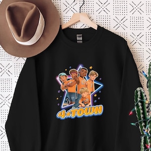 Può includere: Felpa nera con una grafica di quattro ragazzi dei cartoni animati con camicie arancioni in piedi davanti a una stella con il testo "4*TOWN" in lettere gialle e blu.