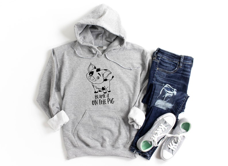 Puede incluir: Una sudadera gris con capucha con un cerdo de dibujos animados en blanco y negro y el texto "Blame it on the pig". La sudadera se combina con jeans azules y zapatillas grises.