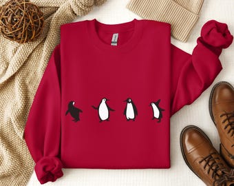 Può includere: Felpa rossa con una grafica di cinque pinguini che camminano in fila. I pinguini sono neri e bianchi con la pancia bianca e le ali nere.