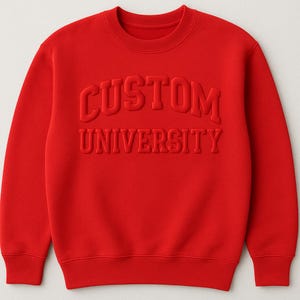 May include: A bright red sweatshirt with the words "CUSTOM UNIVERSITY" embossed across the chest. The crew neck sweatshirt is a solid color, with the text in a slightly darker shade of red.