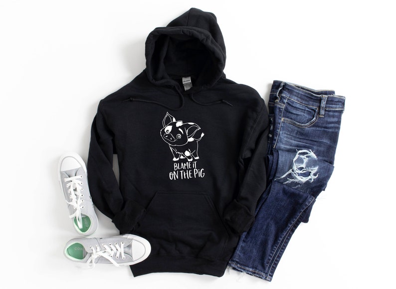 Puede incluir: Sudadera con capucha negra con un cerdo de dibujos animados blanco y el texto "Blame it on the pig".