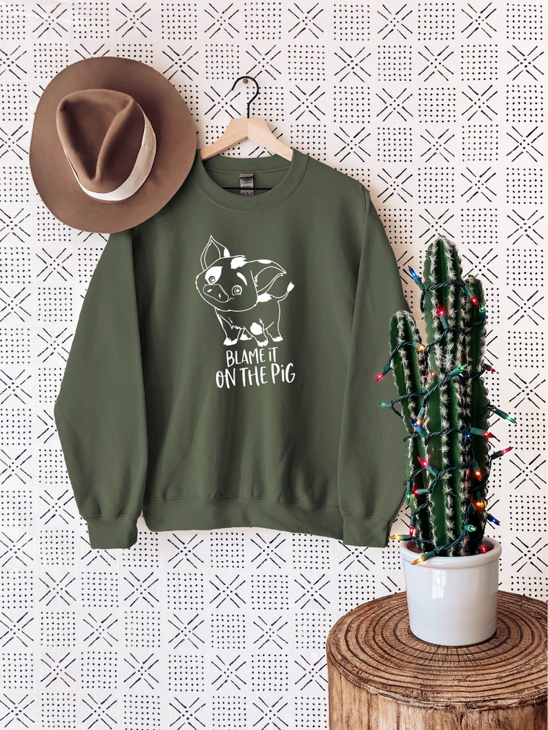 Puede incluir: Una sudadera verde con un cerdo de dibujos animados blanco y el texto "Blame it on the pig".