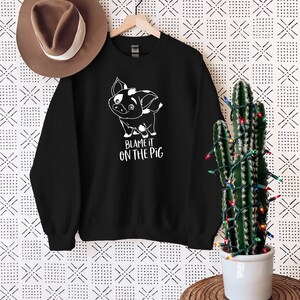 Puede incluir: Sudadera negra con un gr&aacute;fico blanco de un cerdo de dibujos animados y el texto "Blame it on the pig".