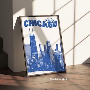 Op de afbeelding: Ingelijste kunstdruk met een blauw-witte illustratie van de skyline van Chicago. Het woord "CHICAGO" staat in vette blauwe letters. De print wordt gepresenteerd op een houten oppervlak.