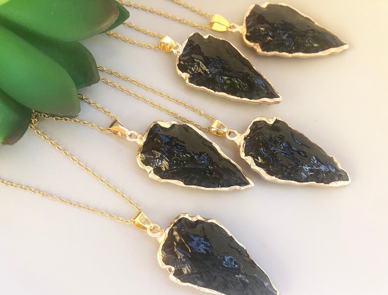 Pode incluir: Cinco colares de ouro com pingentes de ponta de flecha de obsidiana preta. As pontas de flecha s&atilde;o todas de formas e tamanhos diferentes.