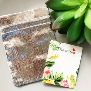 Pode incluir: Uma bolsa prateada com um cart&atilde;o de agradecimento branco com um design floral e o texto "Obrigado" com um cora&ccedil;&atilde;o vermelho.