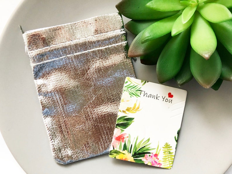 Pode incluir: Uma bolsa prateada com um cart&atilde;o de agradecimento branco com um design floral e o texto "Obrigado" com um cora&ccedil;&atilde;o vermelho.