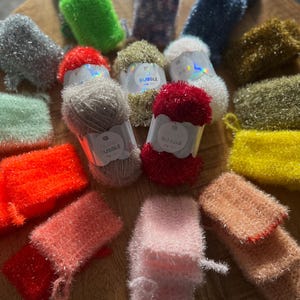 Peut inclure: Un assortiment de pelotes de laine colorées et de torchons à vaisselle tricotés dans différentes couleurs, notamment rose, orange, vert, bleu et jaune. Les pelotes de laine sont étiquetées "Bubble" et les torchons sont fabriqués avec un fil moelleux et texturé.