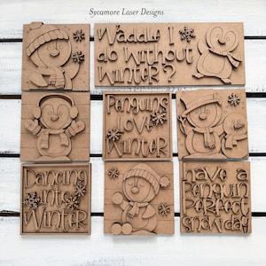 May include: A collection of wooden penguin-themed signs. Each sign features a penguin design and winter-related text, such as "Waddle I do without Winter?" and "Penguins Love Winter." The signs are made of light brown wood.