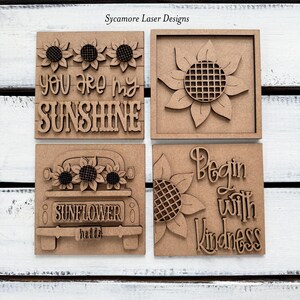 May include: Four wooden decorative squares with sunflower designs and inspirational quotes. One square reads "You are my sunshine," another features a sunflower, a third shows a truck with sunflowers, and the last says "Begin with Kindness."