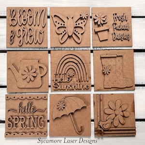 May include: Nine wooden signs with spring-themed designs, including a butterfly, a rainbow, a watering can, a pair of rain boots, an umbrella, a daisy, and text that reads "Bloom & Grow", "Fresh Picked Daisies", "Hello Sunshine", "Hello Spring", and "Sycamore Laser Designs".