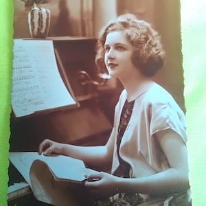 Postal belga sin usar de una joven al piano, con partituras en mano y un hermoso florero encima del piano. los años 30
