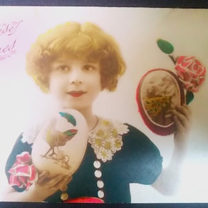 Cartolina francese usata del 1928, raffigurante una ragazza bionda con due uova di Pasqua decorate con un fiore bianco e uno rosso. " Joyeuse Paques"