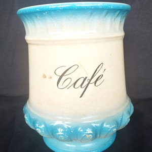 May include: A white ceramic jar with a blue glaze and a decorative design around the top and bottom. The jar has the word "Cafe" written in black cursive on the front.