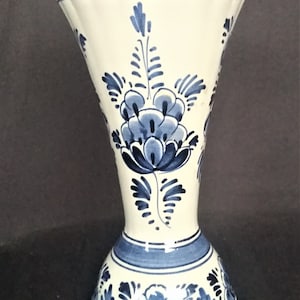 Pode incluir: Um vaso de cerâmica branco com um design floral azul e branco. O vaso tem uma parte superior alargada e uma base larga.