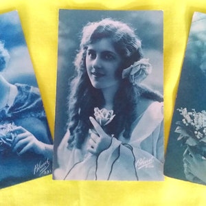 Set van Drie blauwkleurige ansichtkaarten van het Franse merk " Bleuet Paris ", Jongedames met mooie kapsels en bloem in de hand, Meiklokjes