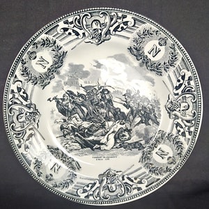 May include: A black and white ceramic plate with a decorative border and a scene of a battle. The plate features the text "Combat de Dennewitz 6. Sept. 1813".