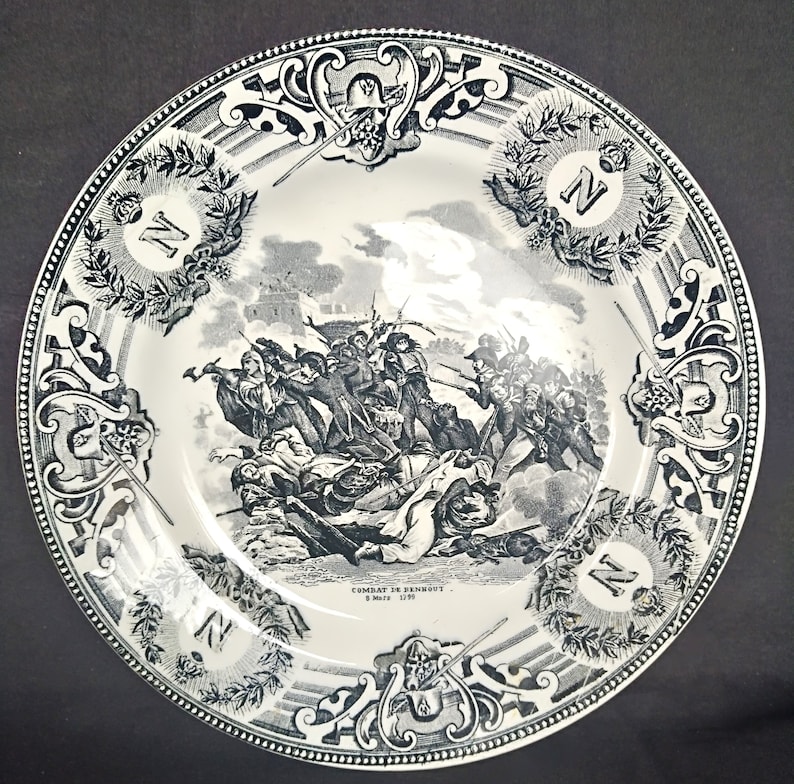 May include: A black and white ceramic plate with a decorative border and a scene of a battle. The plate features the text "Combat de Dennewitz 6. Sept. 1813".
