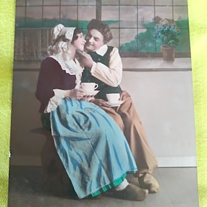 Cartolina francese degli anni '20 raffigurante una romantica coppia di contadini in costumi regionali che sorseggiano una tazza di caffè