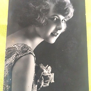 Postal francesa en blanco y negro de la empresa GHR Paris. Representa a una bella dama con un hermoso vestido de los años 20, un hermoso peinado y una flor.