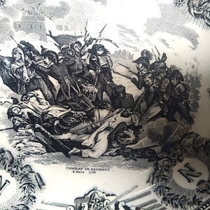 May include: Black and white illustration of a historical battle scene with soldiers fighting. The image is on a white ceramic plate with a black border and the text "COMBAT DE BENNOUT 8 Mars 1799".