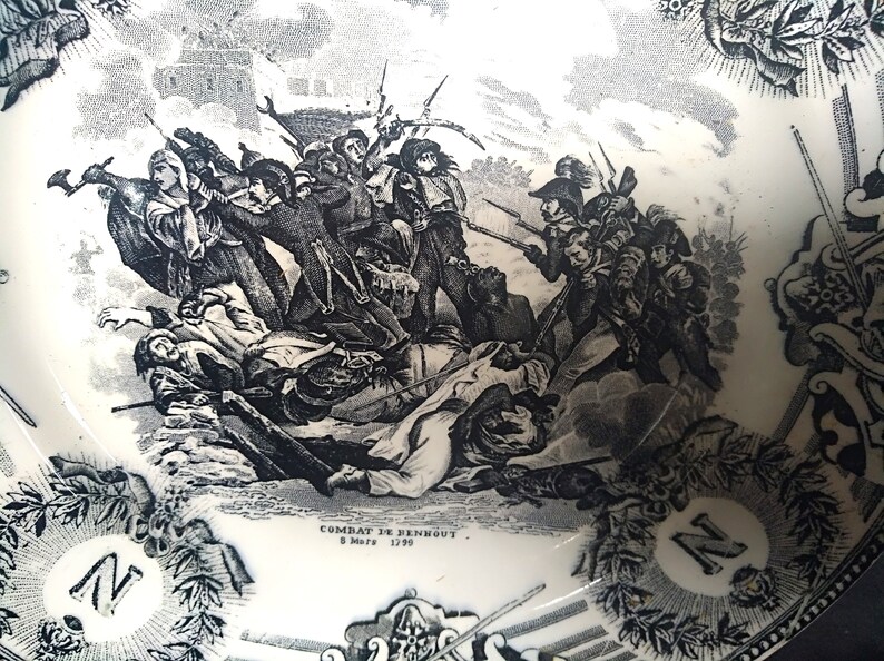 May include: Black and white illustration of a historical battle scene with soldiers fighting. The image is on a white ceramic plate with a black border and the text "COMBAT DE BENNOUT 8 Mars 1799".