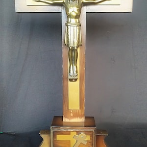 May include: A wooden crucifix with a gold-toned Jesus figure. The crucifix has a base with an anchor and chalice design.