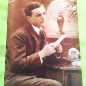 Hombre vestido con un hermoso traje de los años 20, sentado en su escritorio, escribiendo una carta a su amante, al fondo una lámpara art decó y una flor