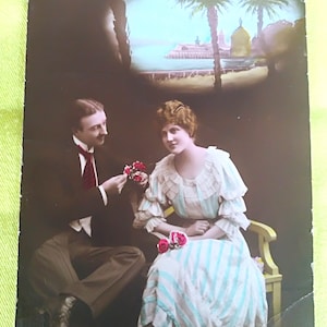 Postal exótica de una pareja romántica profesándose su amor con una escena con palmeras y flores orientales en el medallón superior.