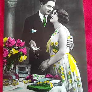 Tarjeta de cumpleaños alemana de principios de 1900, con un hermoso texto en alemán, Pareja enamorada en un interior con mesa y jarrón con ramo de rosas.